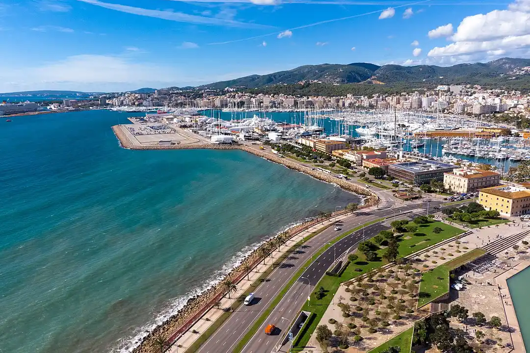 An aerial view of a bustling coastal city port filled with white yachts next to the deep blue sea.