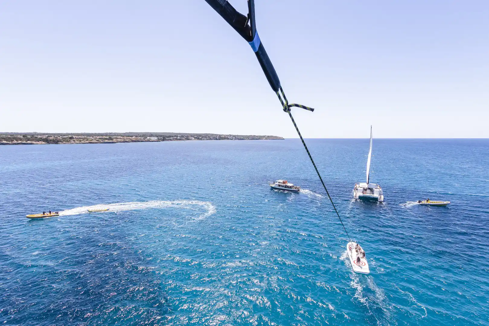 Blick aus der Höhe auf mehrere Boote, die auf einem helltürkisen Meer unter blauem Himmel fahren. Blick aus der Höhe auf mehrere Boote, die auf einem helltürkisen Meer unter blauem Himmel fahren.