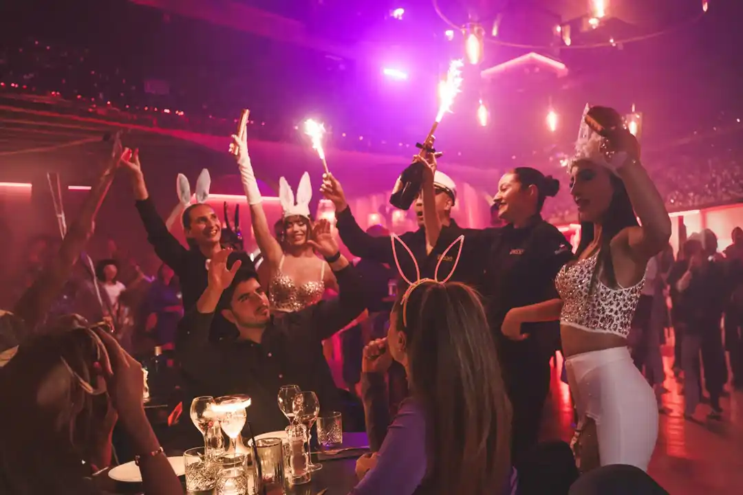 People celebrating with sparklers and bunny ears at a vibrant nightclub party with warm lighting.
