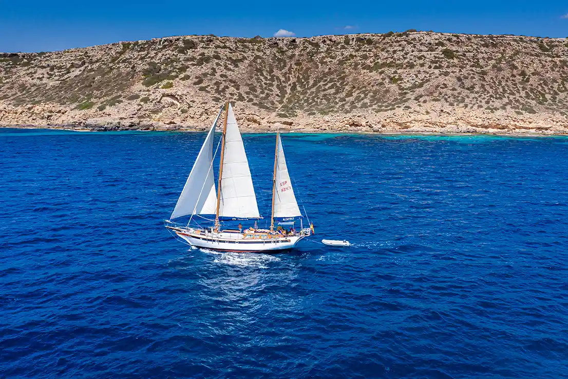 Ein klassisches Segelboot auf blauem Meer neben einer kargen Insel.