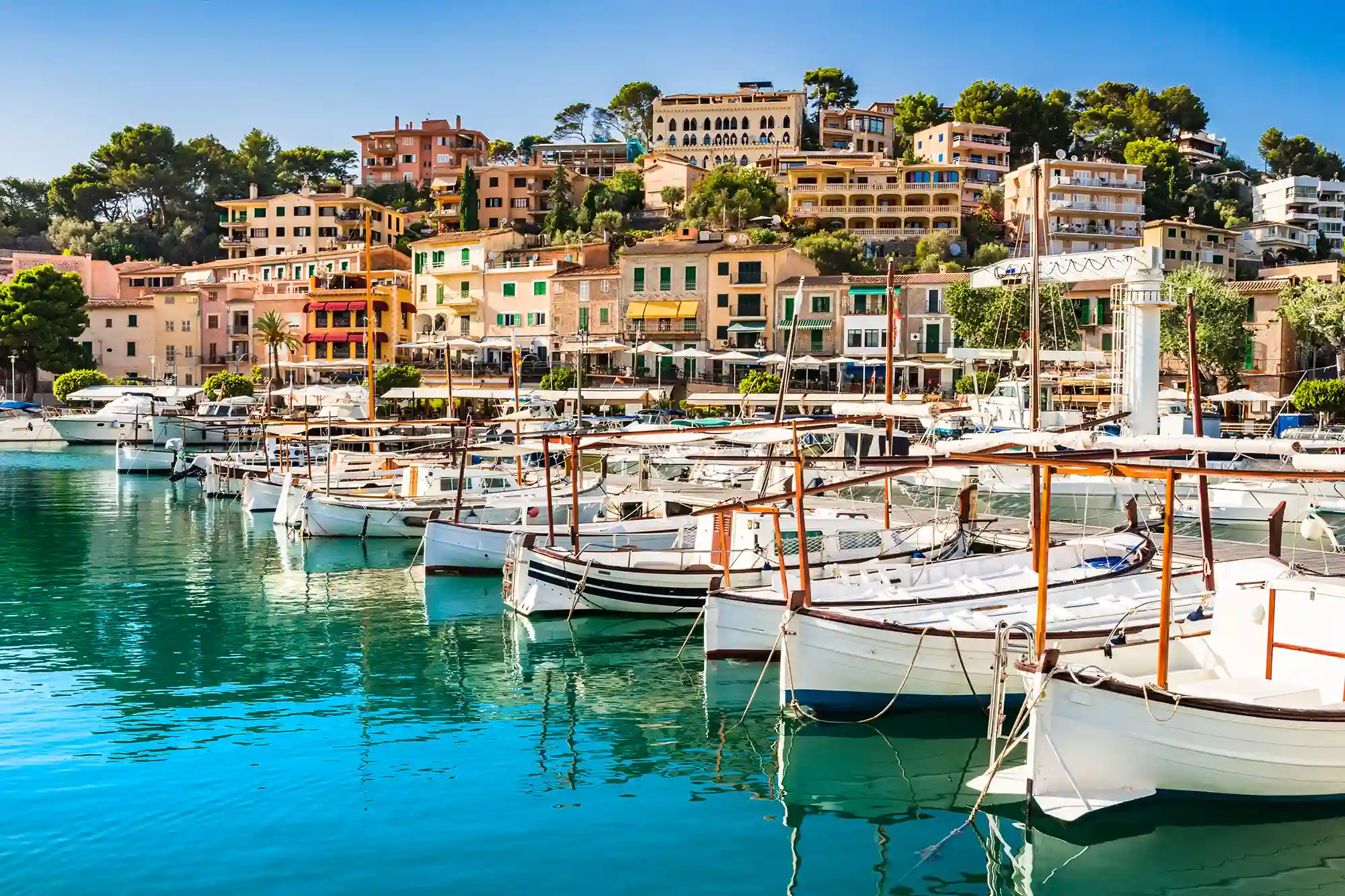 Port de Soller harbor traditional wooden boats Mallorca Traditional wooden llaut boats moored in the turquoise water of Port de Soller harbor with coastal houses on the hillside.