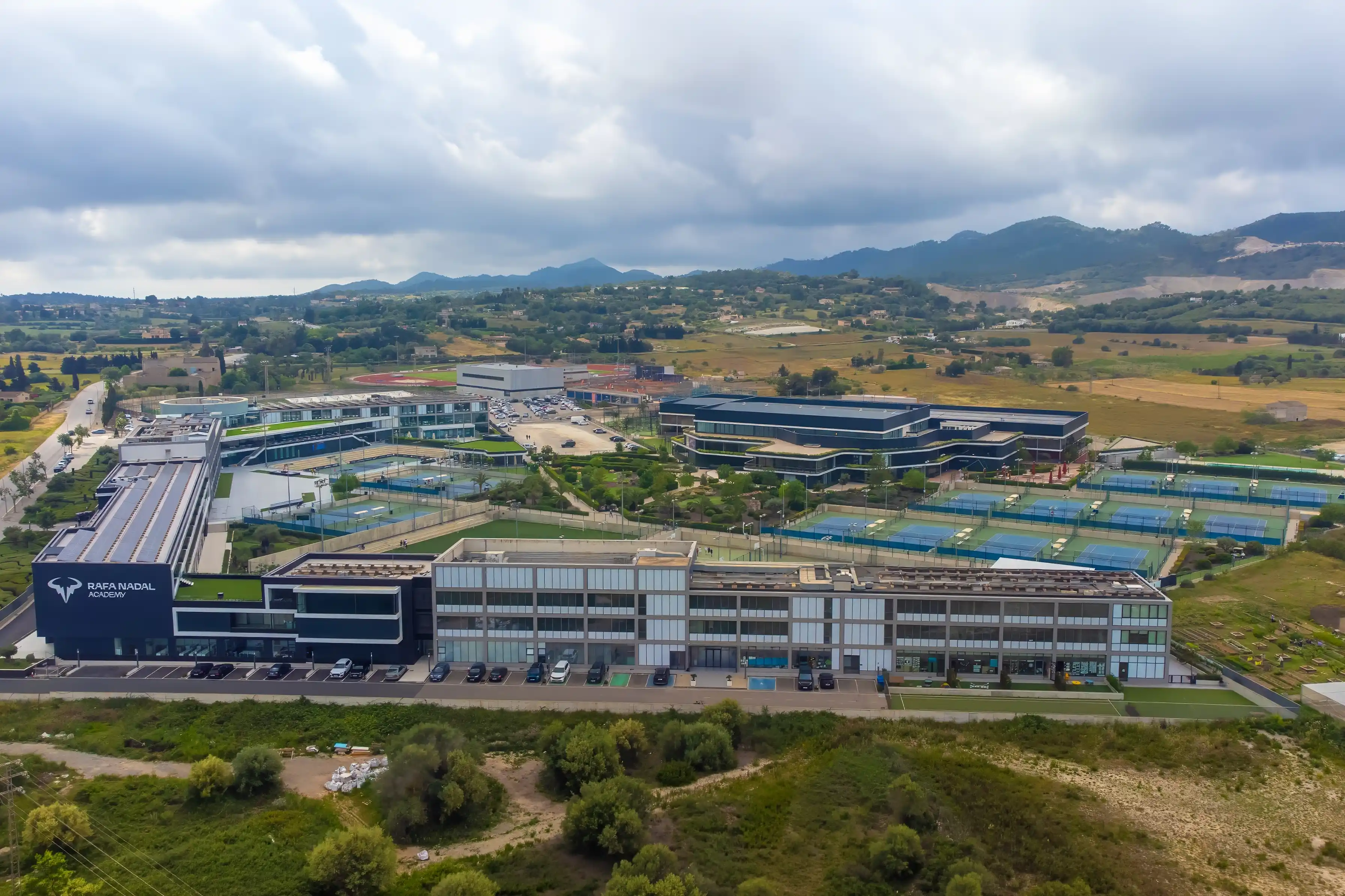 Aerial view of a large sports academy complex with tennis courts surrounded by green hills.