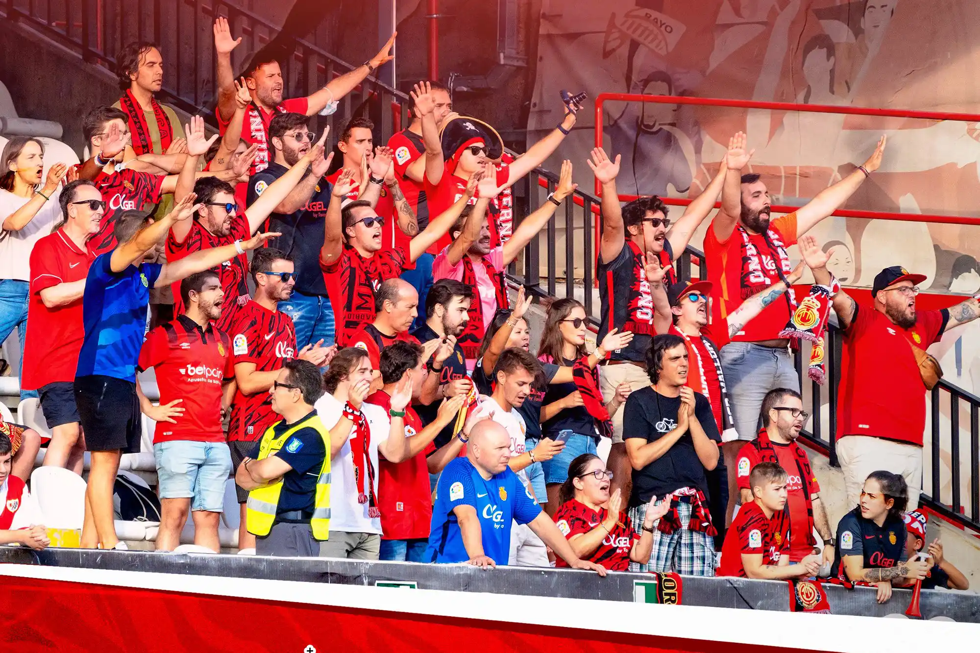 Fußballfans in roten Trikots jubeln mit erhobenen Händen auf den Tribünen eines Stadions. Fußballfans in roten Trikots jubeln mit erhobenen Händen auf den Tribünen eines Stadions.