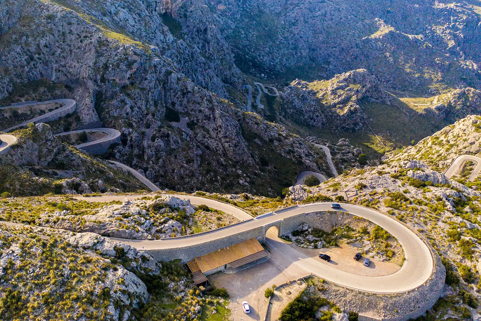 High-angle view of a winding mountain road with a famous loop bridge surrounded by rocky cliffs.