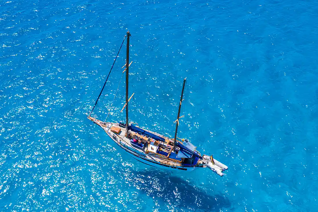 Luftaufnahme eines Segelboots, das im kristallklaren, helltürkisen Meerwasser ankert.
