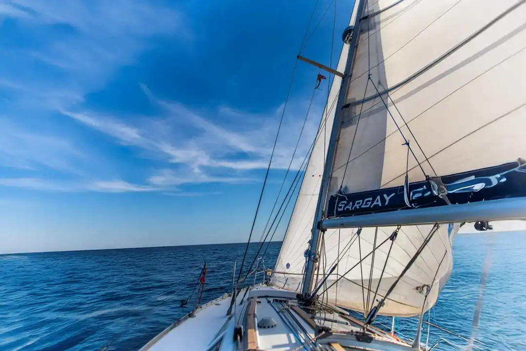 A sailboat cruises through the deep blue sea under a vibrant blue sky with light clouds.