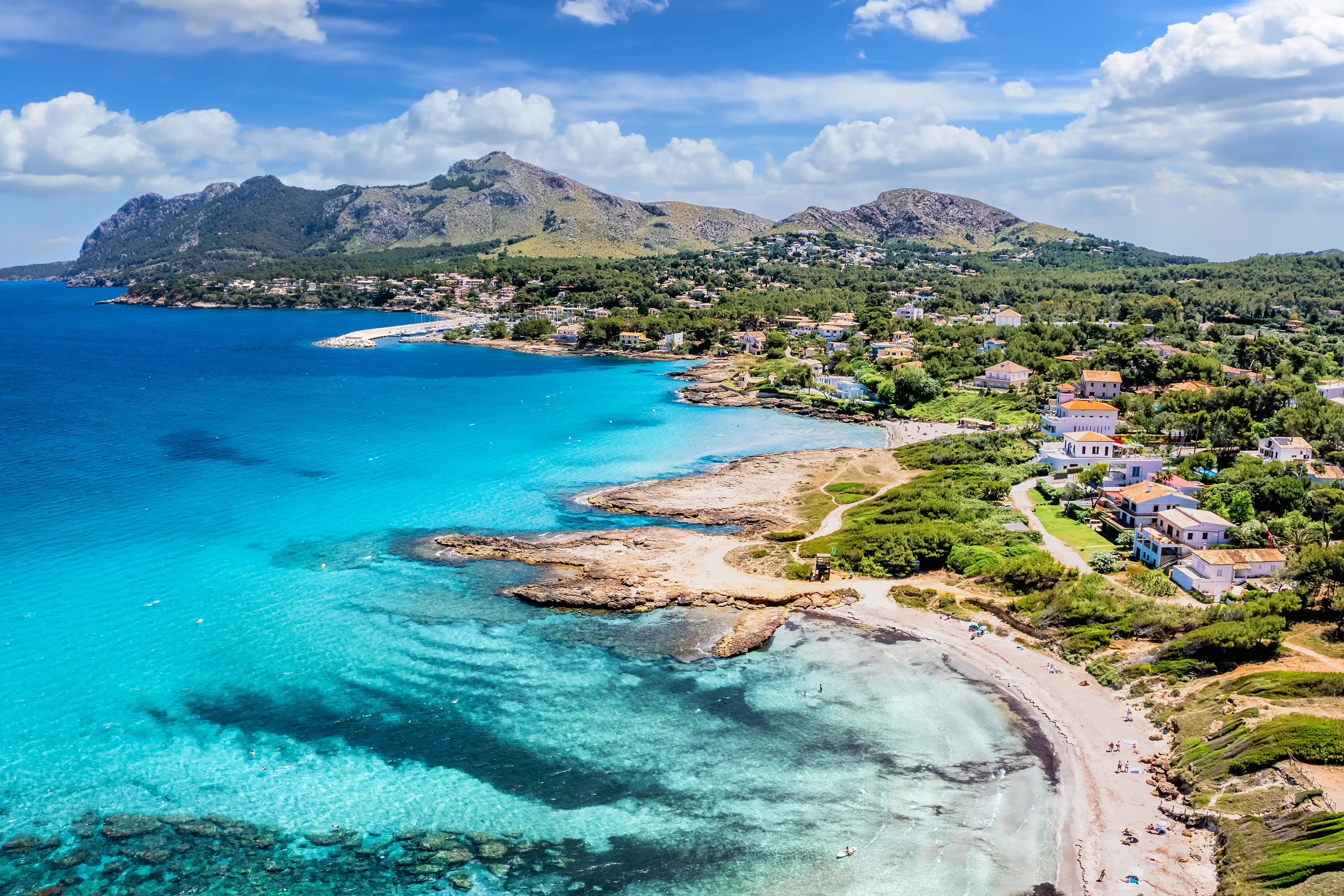 A beautiful view of a turquoise bay with sandy beaches and houses nestled along a green, mountainous coastline.