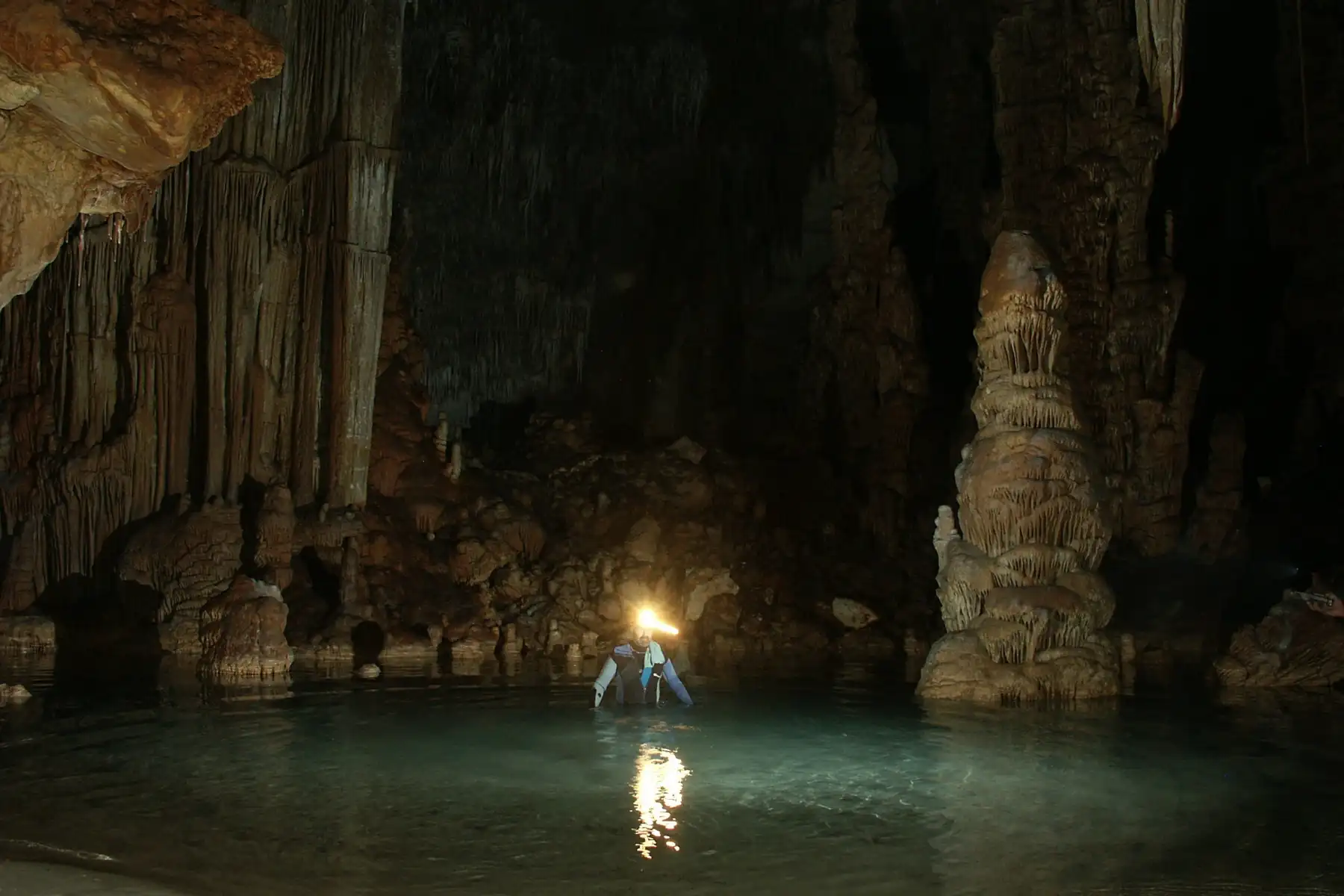 Two people swimming with a flashlight in a dark cave with a subterranean lake and large stalagmites. Two people swimming with a flashlight in a dark cave with a subterranean lake and large stalagmites.