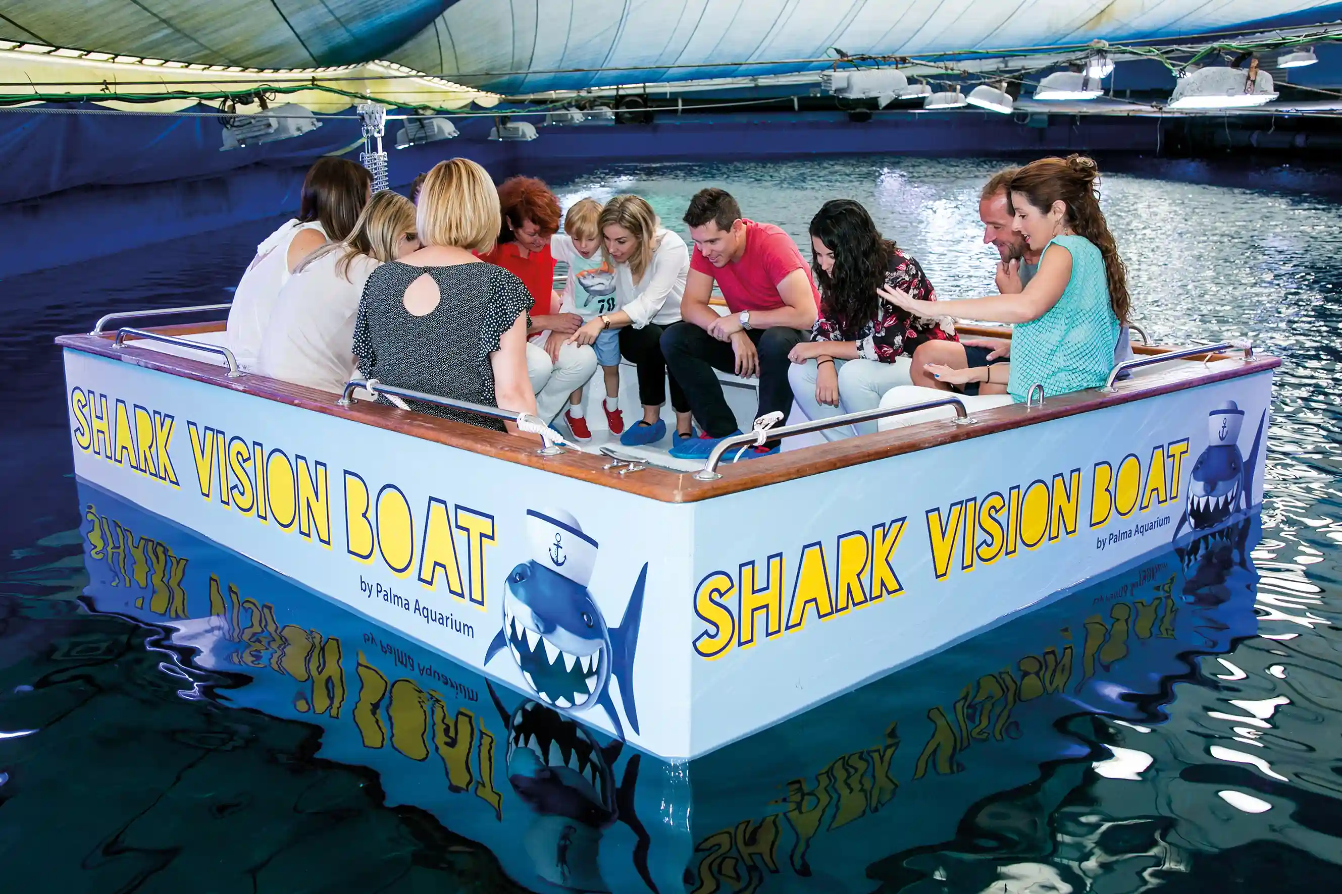 People sitting on Shark Vision Boat in aquarium A group of people sitting together on a Shark Vision Boat inside a large indoor aquarium tank.