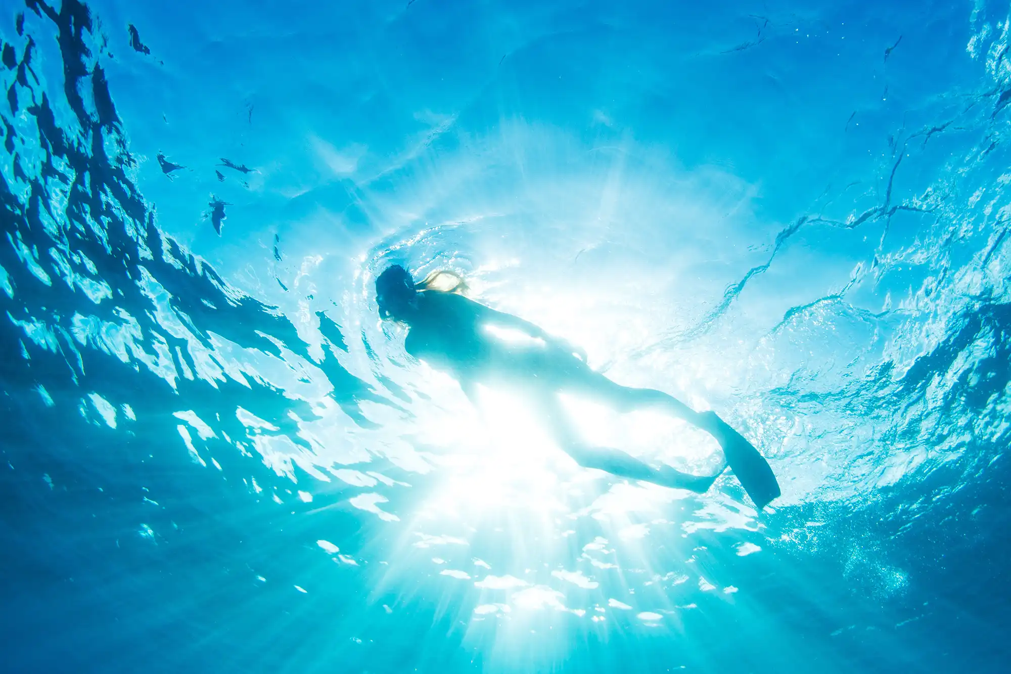 Unterwasseransicht einer Person beim Schnorcheln an der Oberfläche von klarem Wasser mit Sonnenstrahlen. Unterwasseransicht einer Person beim Schnorcheln an der Oberfläche von klarem Wasser mit Sonnenstrahlen.