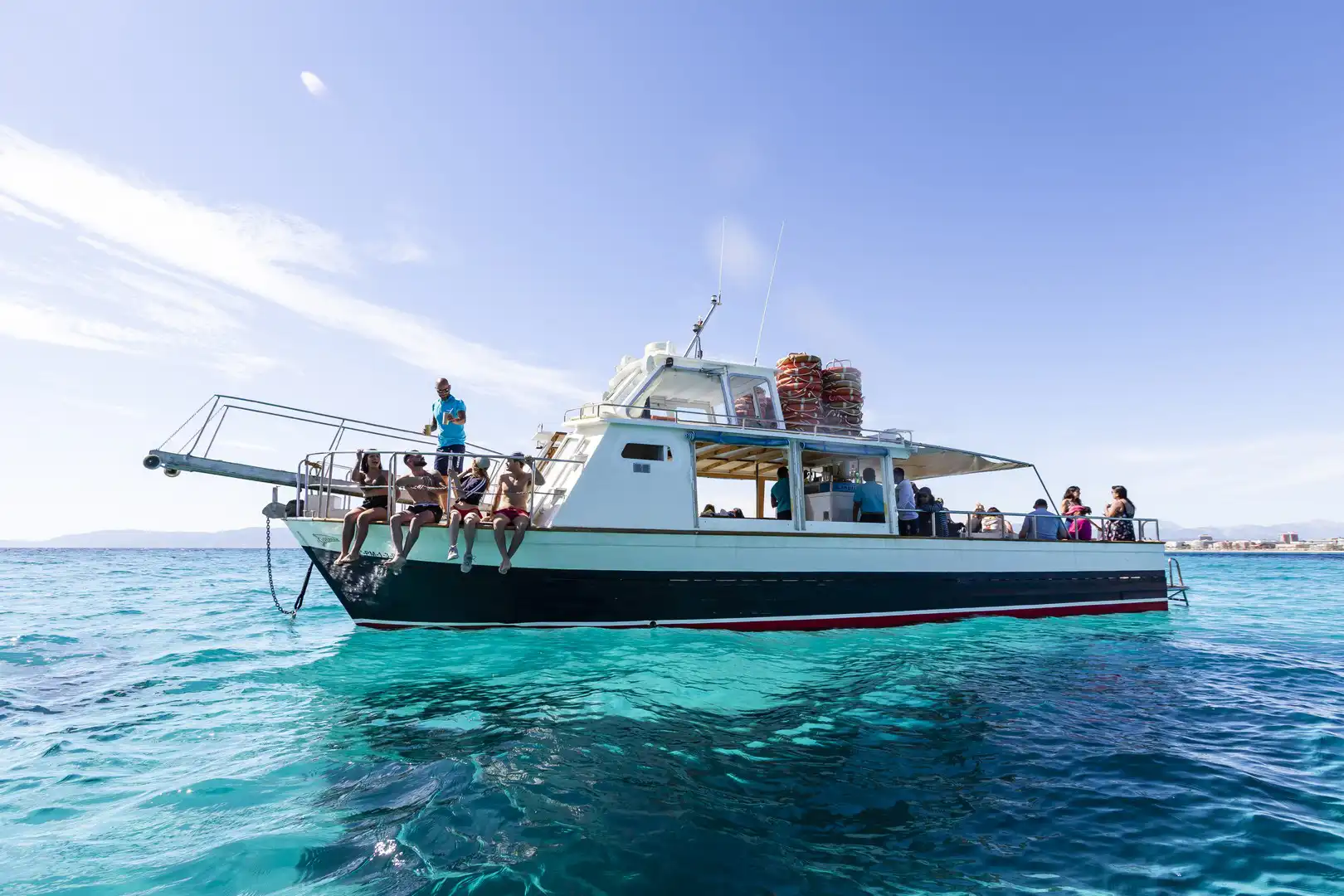 A tourist boat full of people floating on clear turquoise ocean water on a sunny day.