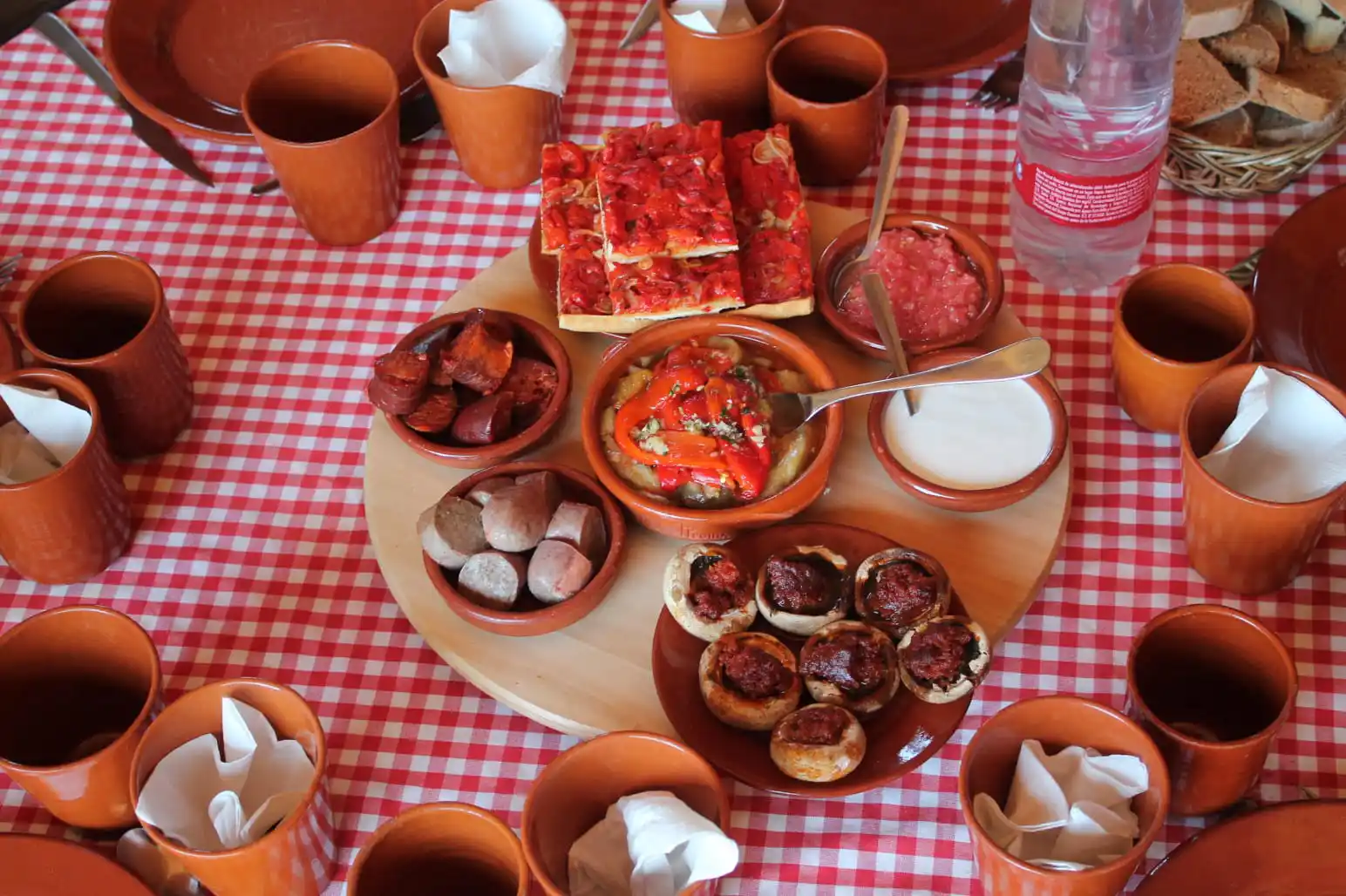 Traditional Majorcan tapas and coca slices served in clay dishes on a red checkered tablecloth.