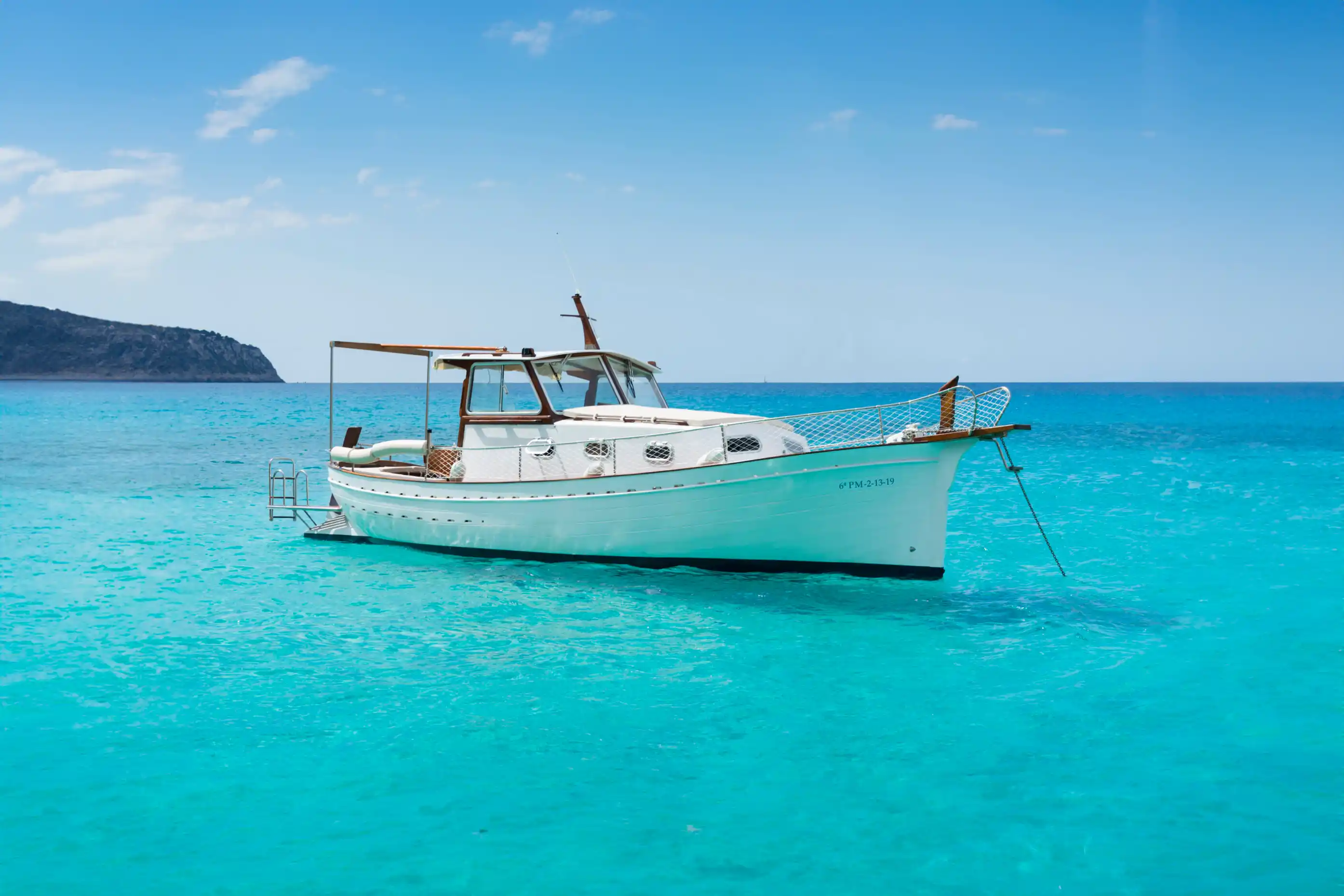 Ein klassisches weißes Boot liegt vor Anker im klaren, türkisfarbenen Meer unter blauem Himmel auf Mallorca.